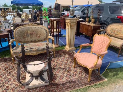 A vintage market scene featuring ornate furniture, including chairs and decorative items, on a patterned rug.