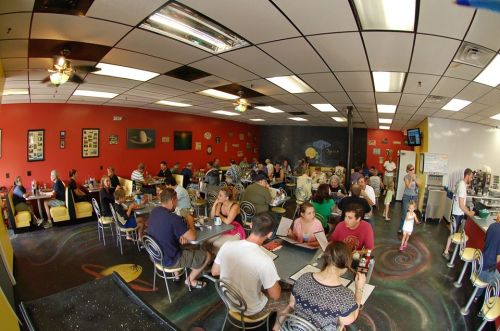 A busy diner with colorful decor, filled with people enjoying meals and chatting at tables.