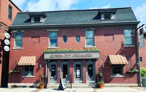 A brick building with a sign reading "Queen City Creamery," featuring awnings and flower pots at the entrance.