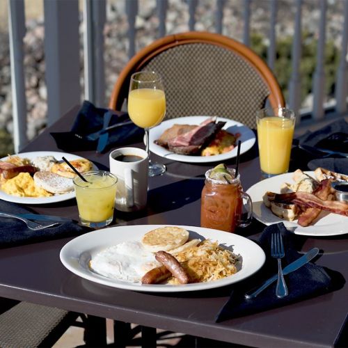 A table set with a variety of breakfast dishes, including eggs, bacon, sausage, and drinks like mimosas and coffee.