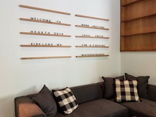 A cozy seating area with a dark sofa and decorative pillows, featuring wooden wall signs with welcoming messages.