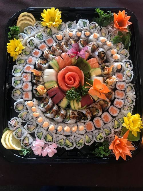 A beautifully arranged sushi platter featuring various rolls, sashimi, and decorative vegetables and flowers.