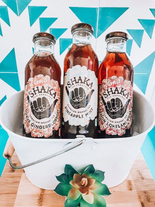 Three bottles of Shaka Hawaiian drinks in a white bucket, featuring flavors: Ginger Blossom, Pineapple Mint, and Lokelani.