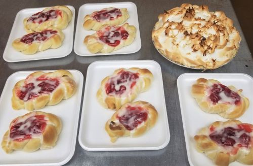 A display of pastries with cherry filling and icing, alongside a pie topped with golden meringue.