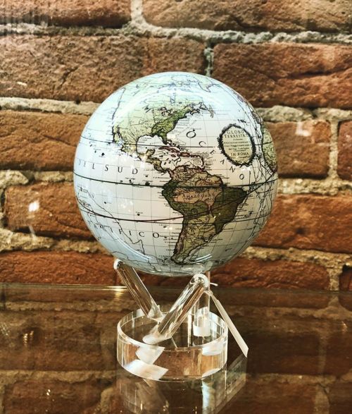 A decorative globe on a clear stand, featuring detailed maps of North and South America against a brick background.