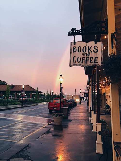 A quaint street scene with a "Books and Coffee" sign, rainbow in the sky, and wet pavement reflecting the evening light.