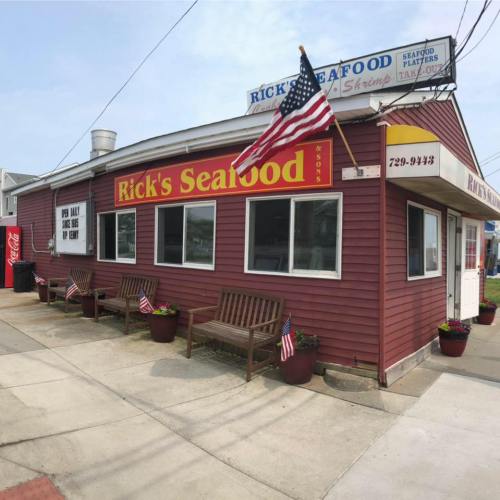 A seafood restaurant with a red exterior, benches, and American flags outside, featuring a sign that reads "Rick's Seafood."
