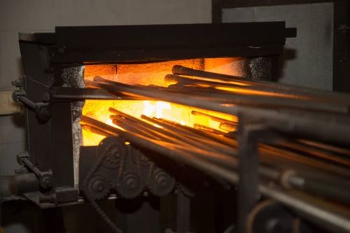 A furnace with glowing orange heat, surrounded by metal rods ready for processing.
