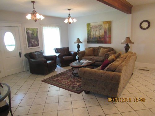 Cozy living room with a sofa, armchairs, coffee table, and decorative lamps, featuring a large window and artwork.