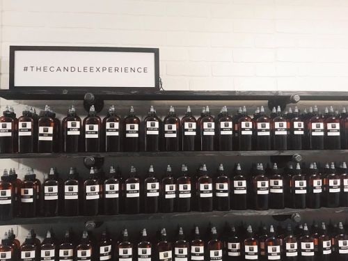 A wall display featuring numerous bottles labeled for a candle-making experience.
