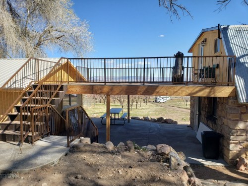 A wooden deck connects two buildings, with stairs leading down to a patio area and a scenic outdoor view.