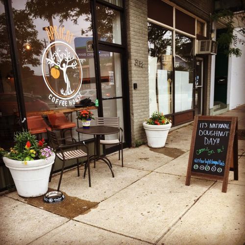 A coffee shop entrance with outdoor seating, flower pots, and a sign promoting National Doughnut Day.