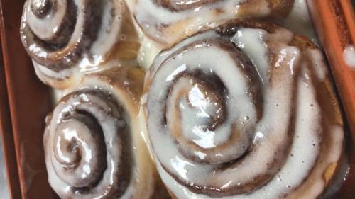 Three freshly baked cinnamon rolls drizzled with creamy icing, arranged in a baking dish.