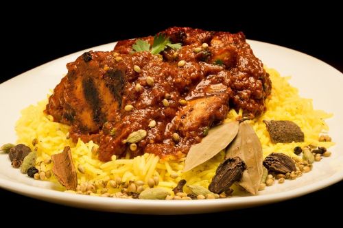 A plate of yellow rice topped with spiced chicken in a rich sauce, garnished with herbs and whole spices.