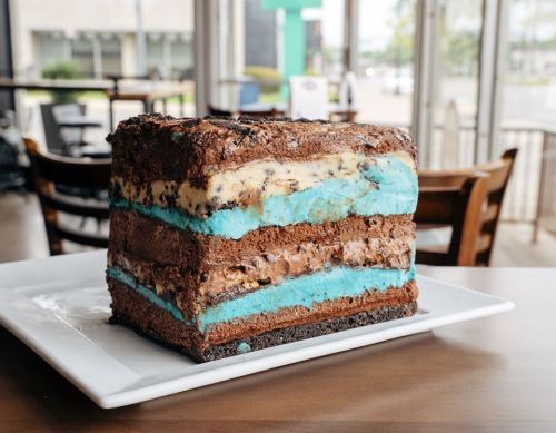A large, layered cake with chocolate, blue, and cream layers, topped with chocolate crumbs, on a white plate.