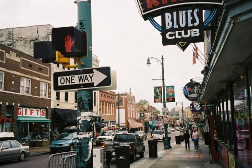A bustling street scene with shops, traffic signs, and a blues club, showcasing urban life and local culture.