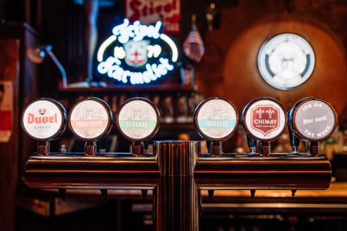 A row of beer taps featuring various brands, with a neon sign in the background.