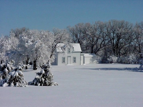 A white house surrounded by snow-covered trees and a vast, snowy landscape under a clear blue sky.