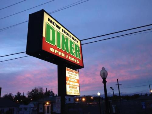 Sign for "New Holiday Diner" with colorful lettering, indicating it's open 7 days, set against a sunset sky.