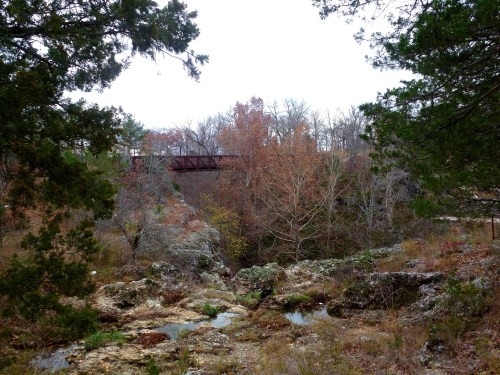 A scenic view of a rocky landscape with a bridge in the background, surrounded by trees and autumn foliage.