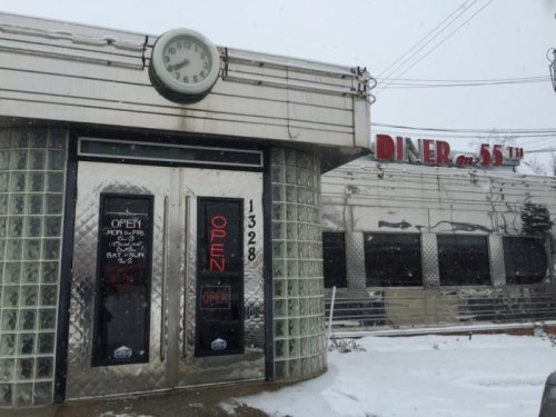 A retro diner with a glass block entrance, neon "OPEN" sign, and a clock, set against a snowy backdrop.