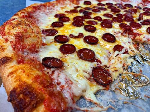A close-up of a pepperoni pizza with melted cheese and a crispy crust, resting on a paper surface.