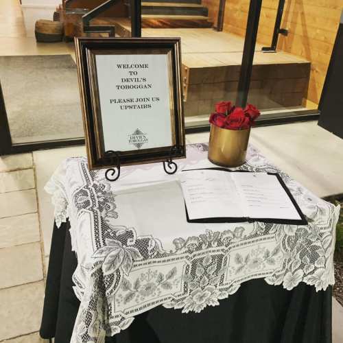 A welcome sign for Devil's Toboggan on a table with a lace tablecloth, roses, and a menu.