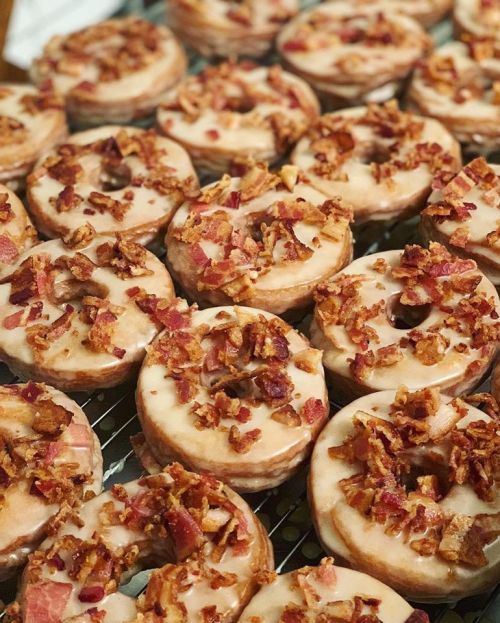 A close-up of glazed donuts topped with crispy bacon bits, arranged neatly on a cooling rack.