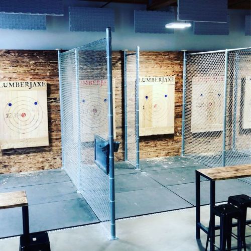 A spacious indoor axe-throwing venue with wooden targets and metal fencing, featuring a rustic wood backdrop.