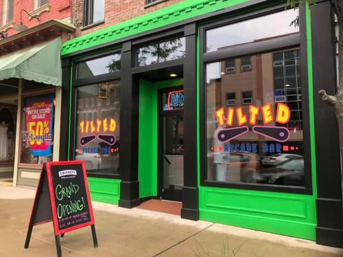 Exterior of Tilted Arcade Bar with colorful signage and a chalkboard announcing the grand opening.