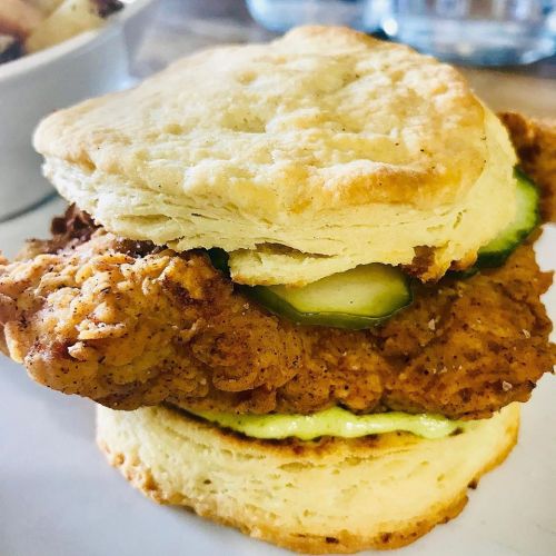 A crispy fried chicken sandwich with pickles and creamy sauce, served on a fluffy biscuit.