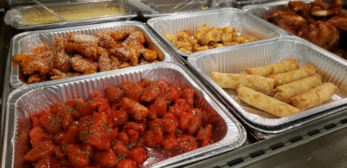 Four trays of various fried foods, including orange chicken, spring rolls, and crispy snacks, arranged neatly.