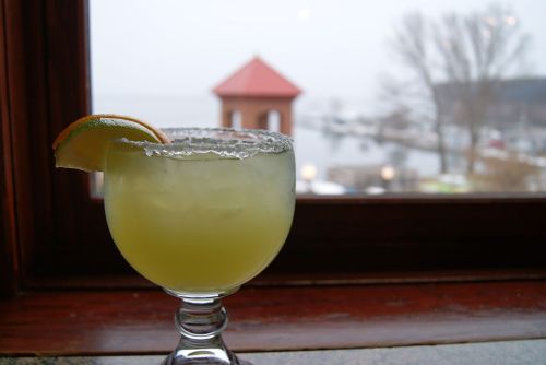 A margarita with a salted rim and lime wedge sits on a windowsill, overlooking a foggy lakeside view.