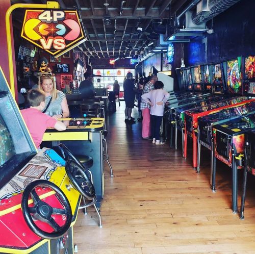 A vibrant arcade with pinball machines and retro games, featuring families enjoying their time together.