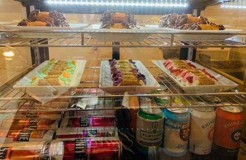 A display case filled with colorful desserts and snacks, including cakes and drinks.