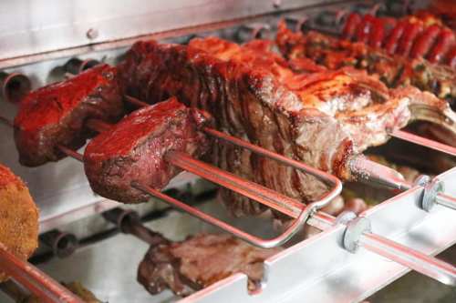 Close-up of various meats on skewers, grilling over an open flame, showcasing a rich, smoky color.