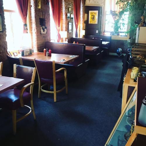 Cozy restaurant interior with wooden tables, chairs, and red curtains, featuring a warm, inviting atmosphere.