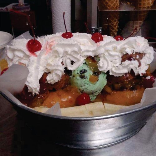 A large banana split topped with whipped cream, cherries, and various ice cream flavors in a metal bowl.