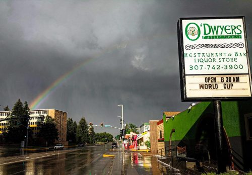 A street scene after rain, featuring a rainbow, a restaurant sign, and wet pavement reflecting the cloudy sky.