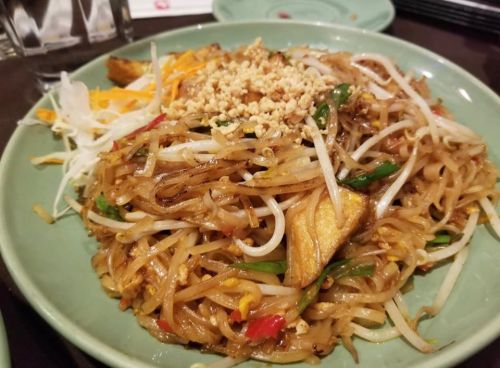 A plate of stir-fried noodles topped with peanuts, bean sprouts, and colorful vegetables.