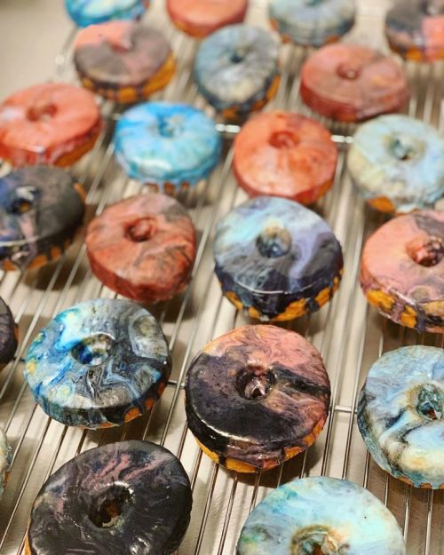 A variety of colorful, marbled donuts arranged on a cooling rack.