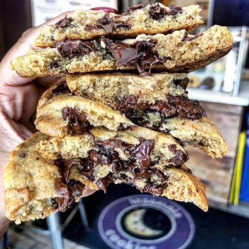 A hand holding a stack of gooey chocolate chip cookies, showcasing melted chocolate and a soft, chewy texture.