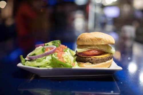 A plate with a burger topped with lettuce, tomato, and cheese, alongside a fresh salad of lettuce, tomatoes, and onions.