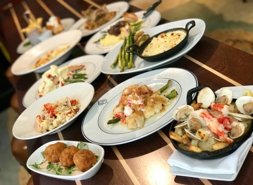 A variety of gourmet dishes arranged on a wooden table, including seafood, vegetables, and appetizers.