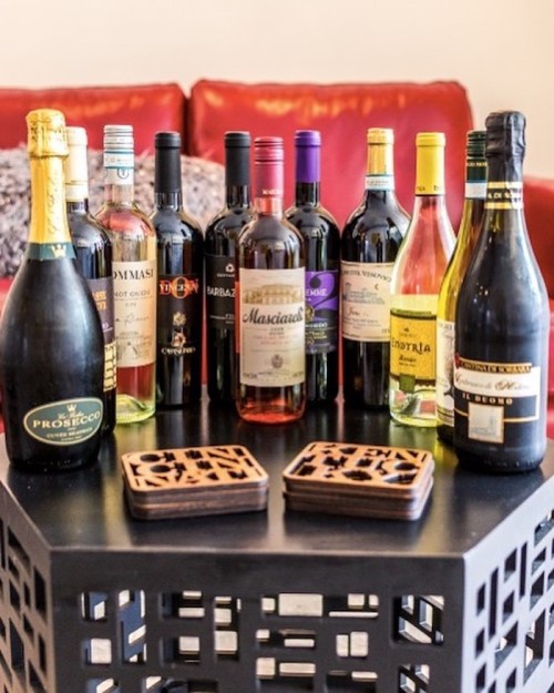 A variety of wine bottles displayed on a black table with coasters, set against a red couch background.