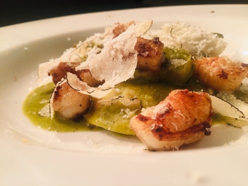 A gourmet dish featuring shrimp, green sauce, and shaved cheese on a white plate.