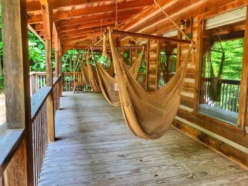 A wooden porch with two hanging hammocks surrounded by greenery.