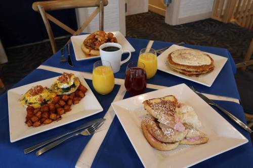 A table set with a blue tablecloth featuring breakfast dishes: pancakes, French toast, eggs, potatoes, and drinks.