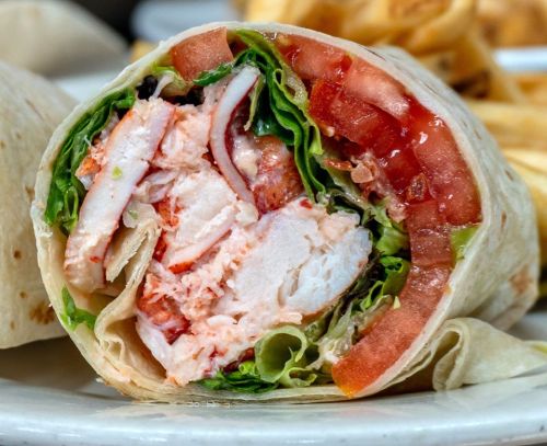 A close-up of a sliced wrap filled with chicken, lettuce, tomatoes, and other ingredients, served on a plate.