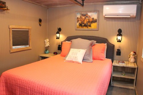 Cozy bedroom with a pink quilted bed, nightstands, wall art, and warm lighting.
